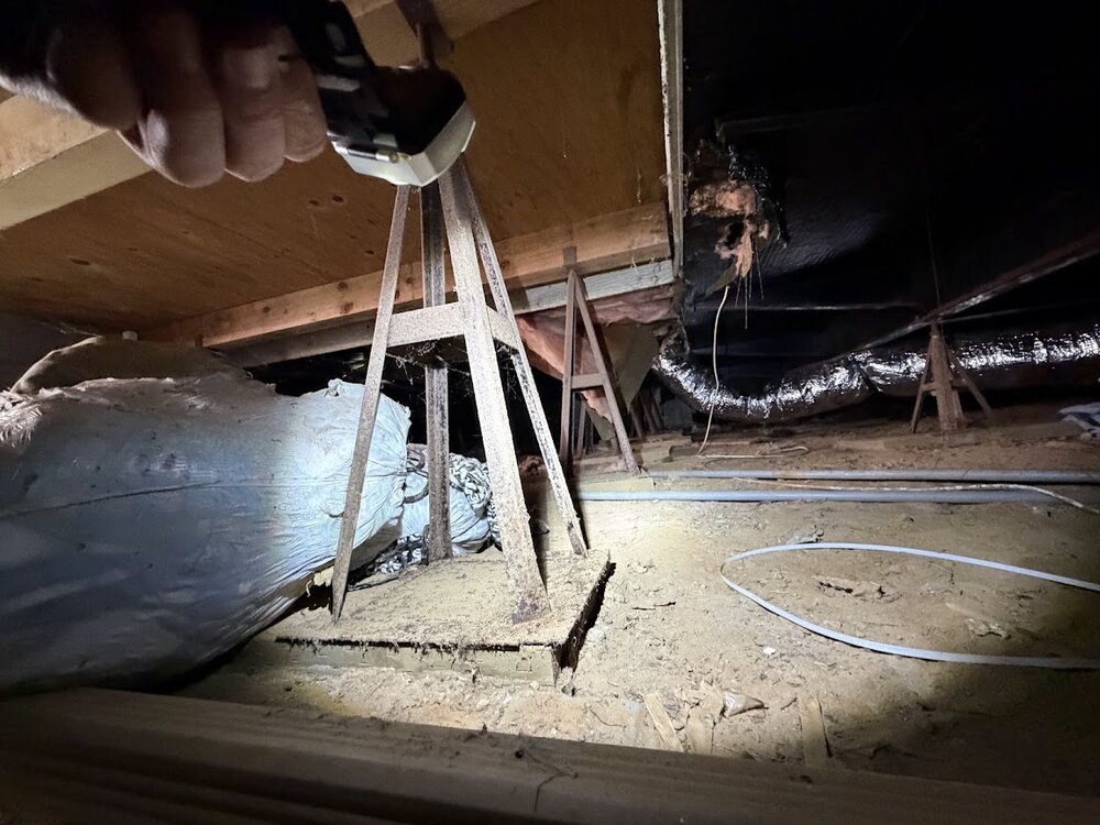 Crew member inspecting under-home framing and support piers with a work light